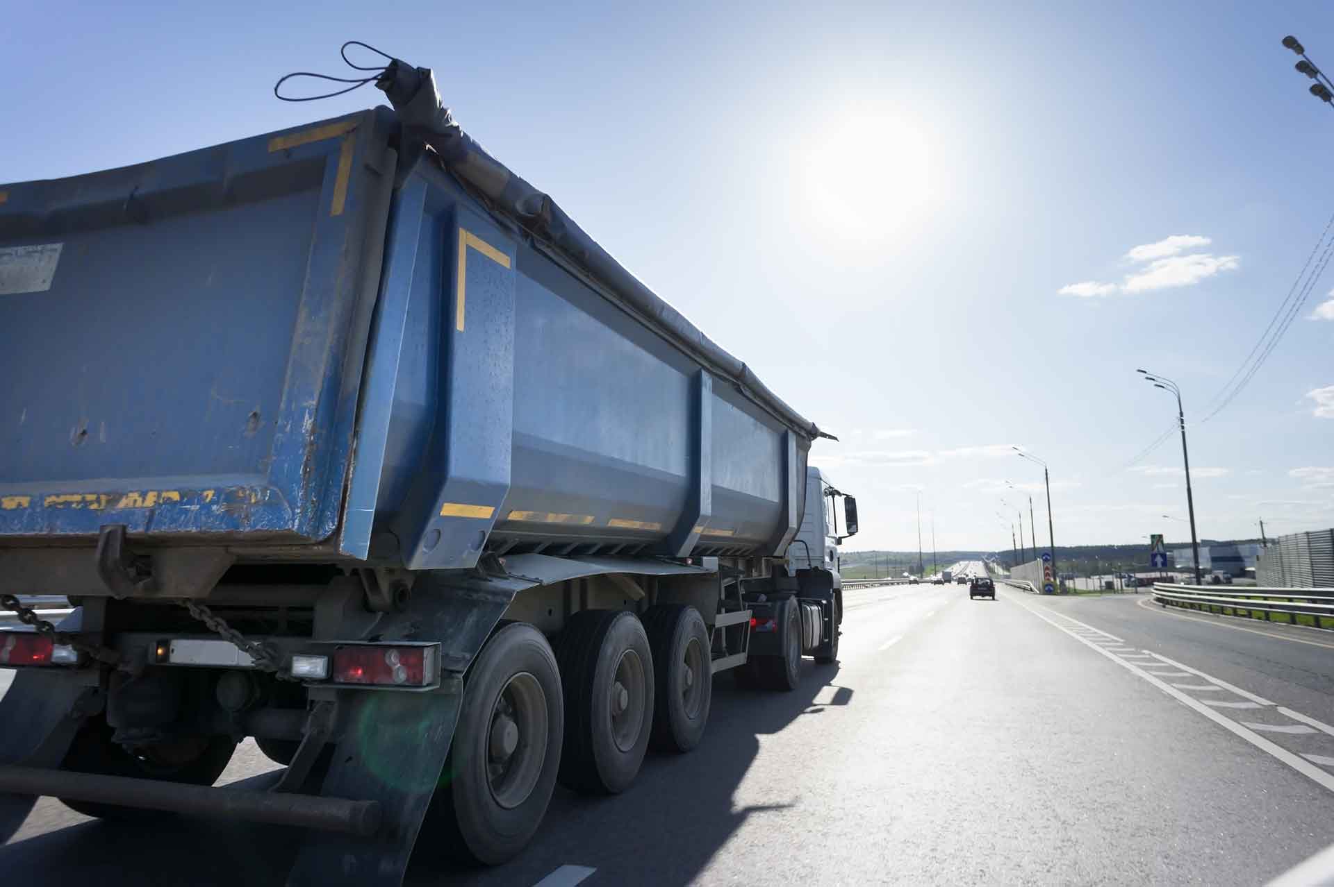 A dumpster truck driving down the road on a sunny day